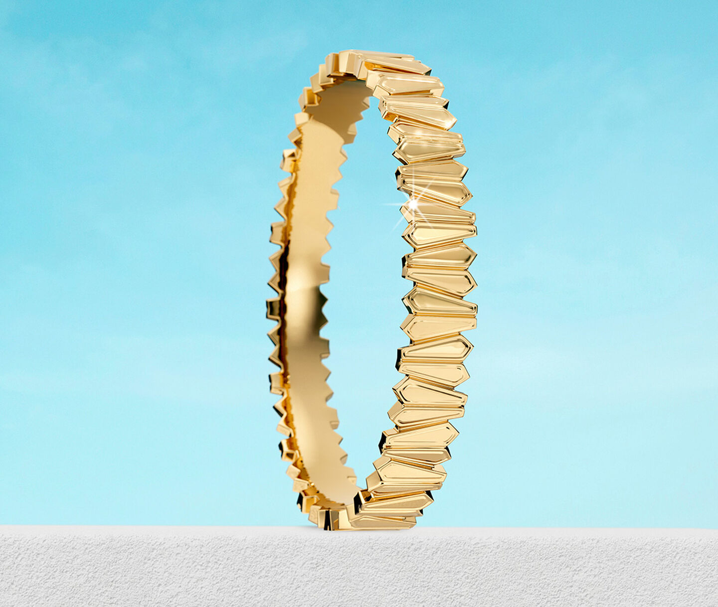 Birks Beekeeper yellow gold bangle on a sky background.